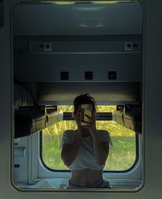 a woman sitting on a train looking out the window at the grass outside her seat