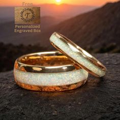 two gold wedding bands with opalite inlays on top of a mountain