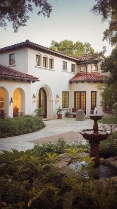 a house with a fountain in front of it and landscaping around the outside area on either side