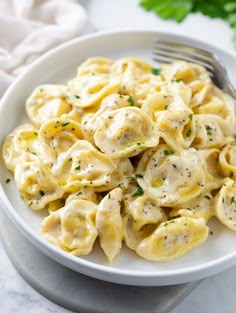 a white bowl filled with pasta covered in sauce and garnished with parsley