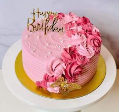 a pink birthday cake with gold lettering and flowers on top is sitting on a white table