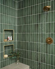 a green tiled bathroom with gold fixtures and shelves on the wall, along with a shower head