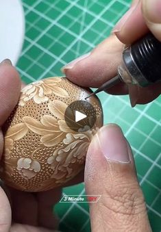 someone is painting an egg with gold and white flowers on the outside, while another person holds it in their hand