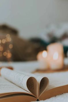 an open book sitting on top of a bed next to two candles and a teddy bear