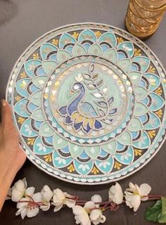 a hand holding a decorative plate on top of a table next to flowers and glasses