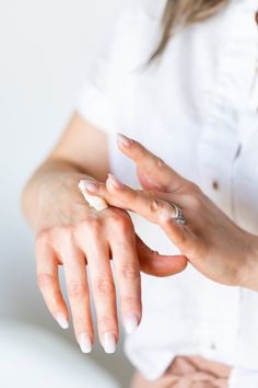 a woman is holding her hand out to touch the nail polish on her nails, while wearing a white shirt