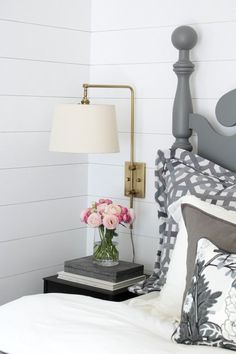 a bedroom with white walls and gray bedding, flowers on the nightstand next to it