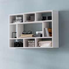 a white shelf with books and other items on it against a blue wall in a room