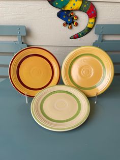 three colorful plates sitting on top of a table next to a chamelon sculpture