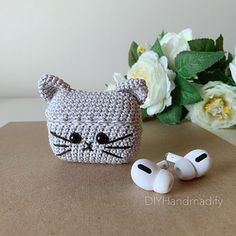 there is a crocheted cat head and earbud holder on the table