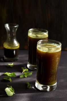 two glasses filled with liquid sitting next to each other on a table covered in leaves