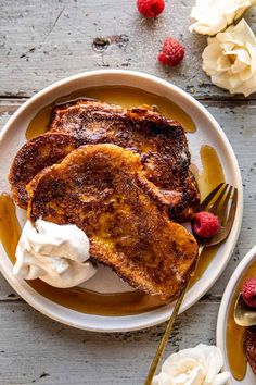 french toast with whipped cream and raspberries on a white plate next to flowers