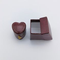 a small wooden box with a heart shaped ring in it next to a leather case