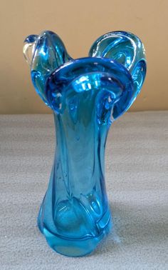 a blue glass vase sitting on top of a white carpeted floor next to a wall