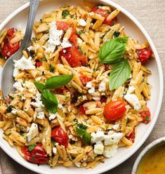 a white bowl filled with pasta, tomatoes and feta cheese on top of a table