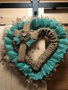 a heart shaped wreath with a cross hanging on the front door, decorated with burlap