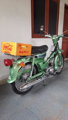 a green motorcycle parked next to a building with a coca cola box on the back