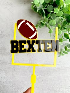 a hand holding up a sign that says bextten with a football on it