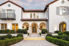 a large white house with lots of windows and bushes in front of it on a sunny day