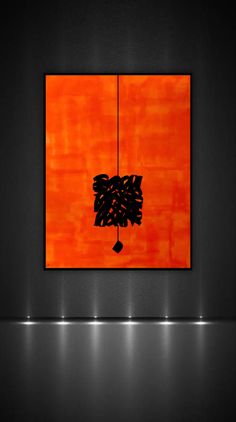 an orange and black painting hanging on a wall in a dark room with lights around it