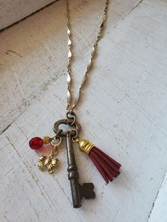 Unique, repurposed vintage skeleton key is the pendant of this necklace.  The key is a vintage skeleton key, with really cool charms attached including a burgundy suede tassle, a gold tone bow charm, and a gorgeous burgundy glass faceted bead charm.  The necklace is about 25 inches long of vintage gold metal chain, with a 3 inch extender chain, making this necklace adjustable up to 28 inches.  The key pendant is 3 inches long.  One-of-a-kind, you will love it! Old Key Necklace, Vintage Key Necklace, Vintage Gold Necklaces With Keys, Vintage Gold Key Necklace, Antique Gold Necklaces With Two Keys, Gold Brass Necklace With Keys, Skeleton Key Crafts, Key Necklace Vintage, Key Charm Necklace