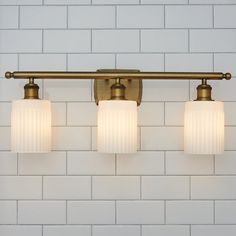 three lights are hanging on the wall next to a white brick wall in a bathroom