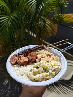 a person holding up a paper plate with food on it and chopsticks sticking out of it