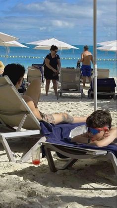 a man laying on top of a beach under an umbrella next to another person in a chair