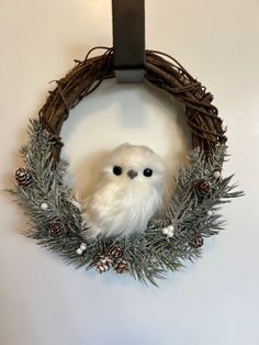 a white owl sitting in a wreath with pine cones on the front and back sides