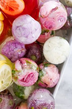 an assortment of different colored flowers in a white bowl on a marble counter top with water droplets over them