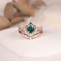 a close up of a ring with a green stone and pearls on the bottom, sitting on a white surface