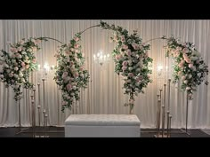 an arrangement of flowers and greenery on display in front of a white curtained backdrop