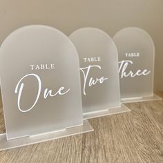 three clear acrylic signs with white writing on them that say table, one two three