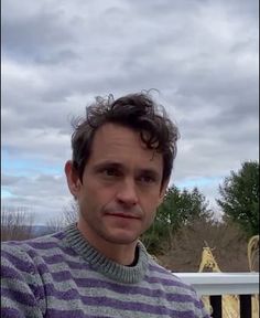 a man with curly hair wearing a purple and white striped sweater looking at the camera