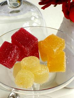 three pieces of gummy bears in a glass bowl next to a vase with flowers