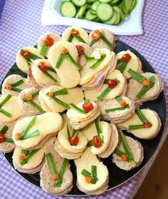 a black plate topped with sandwiches and veggies on top of a purple checkered table cloth