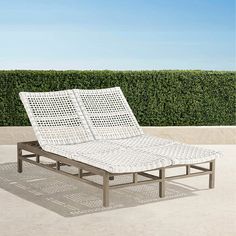 a white lounge chair sitting on top of a cement floor next to a green hedge