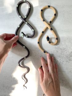 two hands are holding string art pieces on a white counter top, one is black and the other is brown