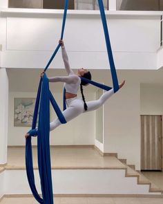 a woman is doing aerial acrobatics in the middle of a room with stairs