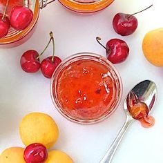 some cherries and lemons on a table next to jars with jam in them