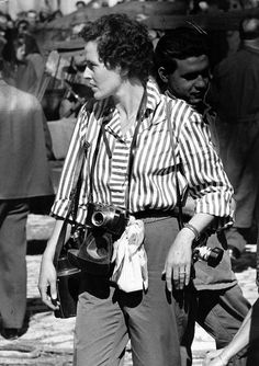 black and white photograph of woman with camera in hand walking down the street while other people look on