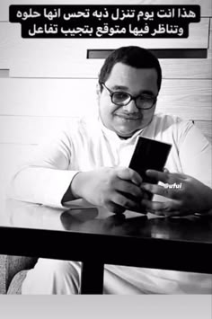 a man sitting at a table with a cell phone in his hand and an advertisement on the wall behind him