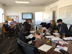 a group of people sitting around a table with papers and pens on it in an office setting