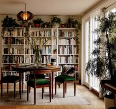 a dining room table surrounded by bookshelves and plants