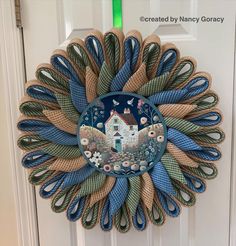 a blue and green wreath with a house on the front door is hanging on a white door