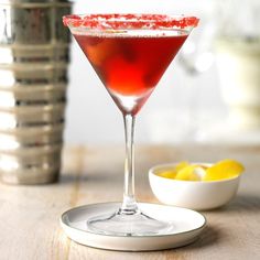 a red drink sitting on top of a table next to a bowl of lemons