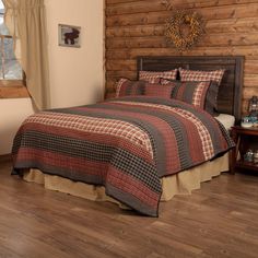 a bed in a room with wooden walls and wood flooring that has a plaid comforter set on it