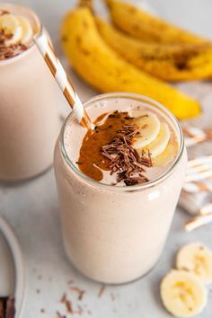 two glasses filled with smoothie next to banana slices and chocolate shaving on the rim