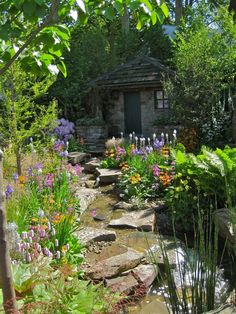 a garden filled with lots of different types of flowers and plants next to a small building