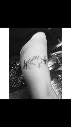 a black and white photo of a mountain with trees on it's side tattoo